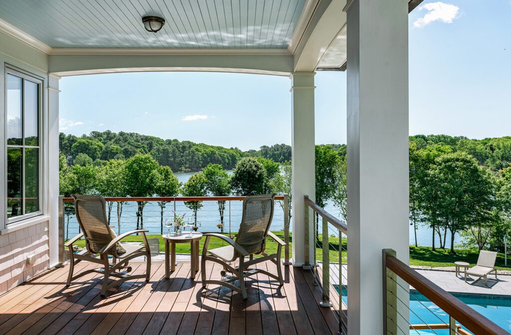 Scenic lakefront deck with cozy seating area, offering a relaxing view of lush green trees and serene water, perfect for outdoor leisure and unwinding by the pool at a home designed by TMS Architects.