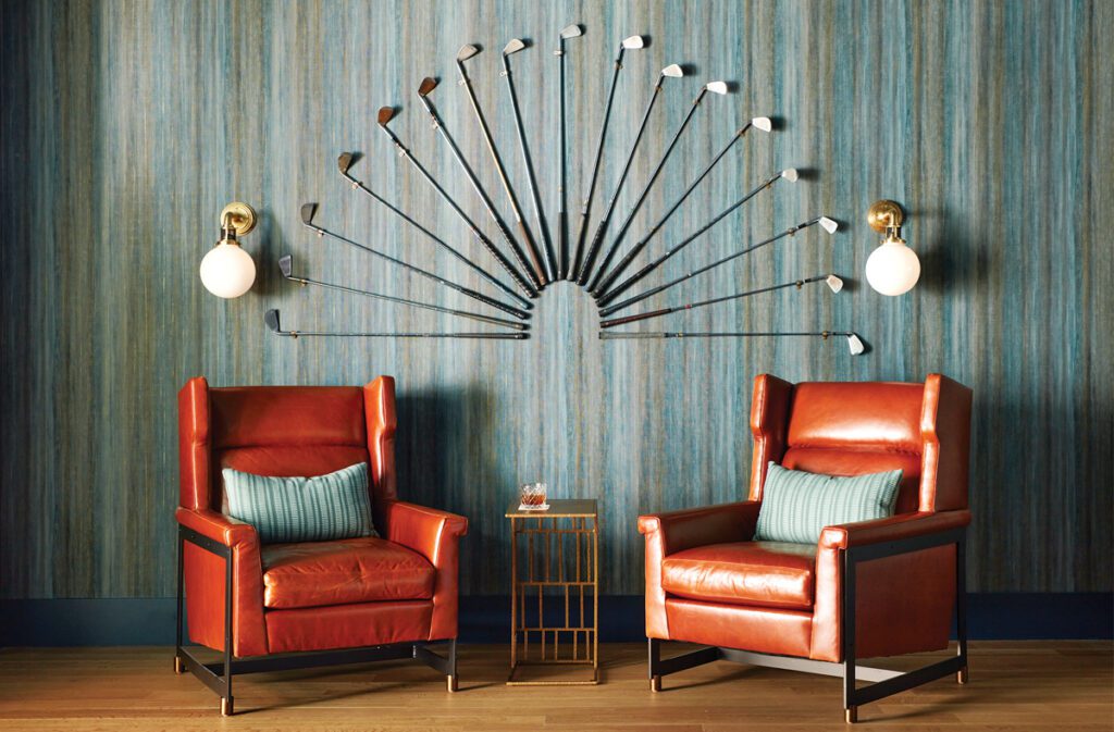 Seating area in a recreation room with two leather chairs and a collection of golf clubs on the wall.