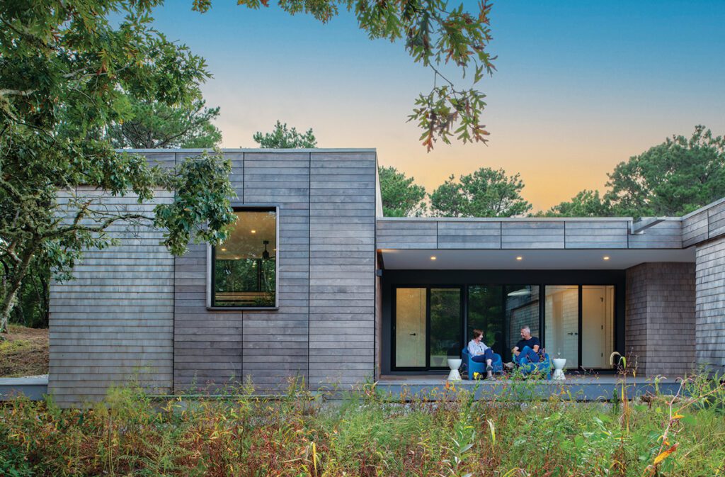 Contemporary cedar-clad home with clean lines, large glass doors, and a covered patio surrounded by native landscaping