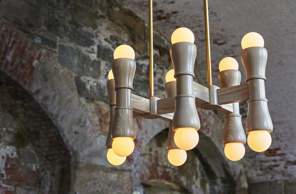 Sculptural wood chandelier with glowing bulbs in a rustic stone setting