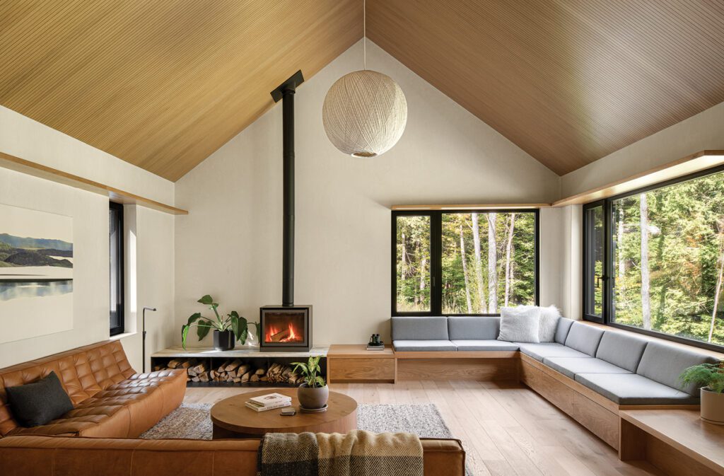 Modern living room with built-in seating, wood ceiling, fireplace, and forest views.
