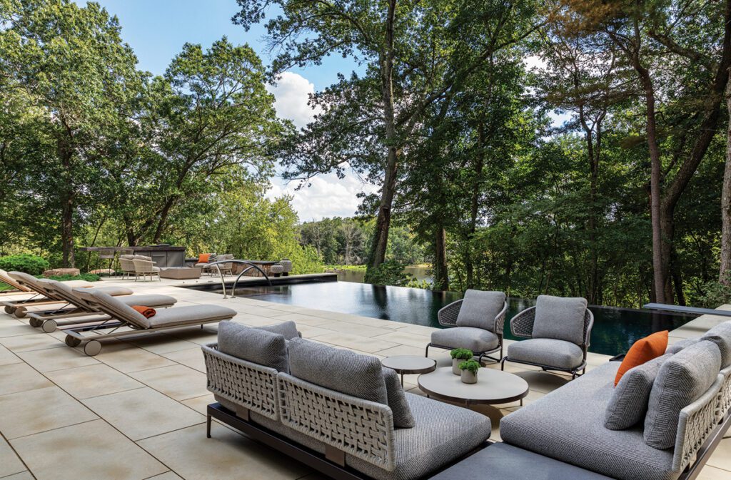 Contemporary outdoor lounge seating area beside infinity pool with woven sofas and forest views.