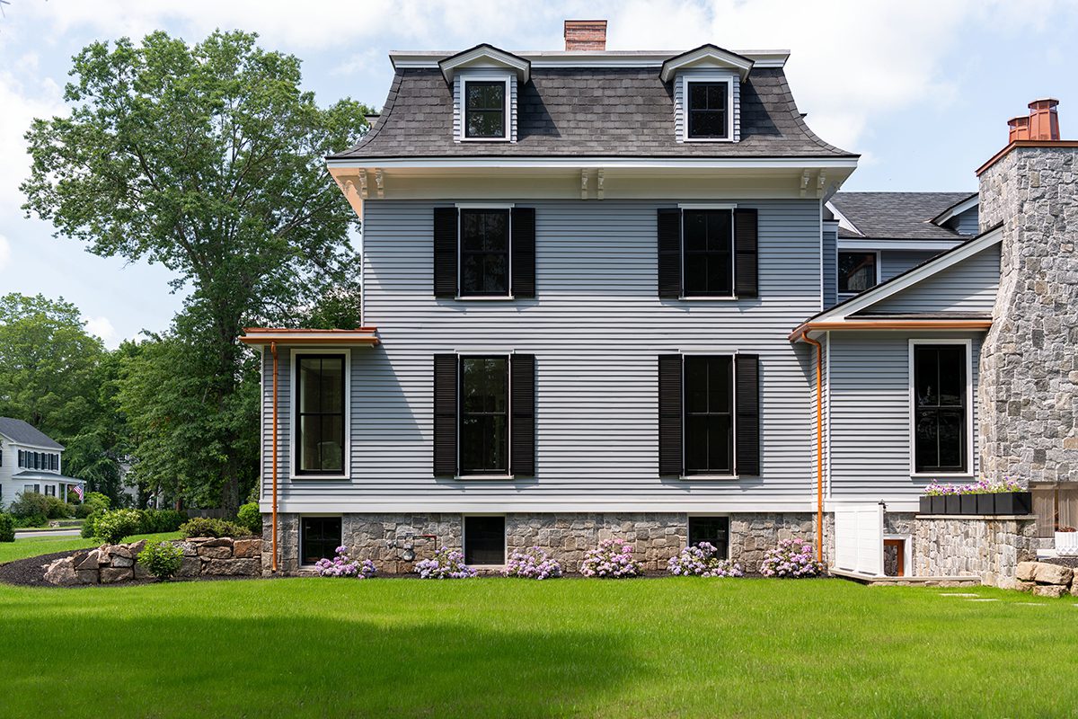 Historic-style New England home with gray siding, black double-hung windows, and stone foundation.